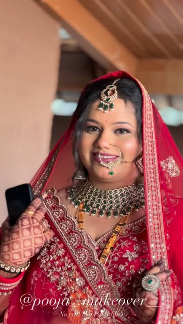 Smiling bride in a red veil with defined eyes, bridal jewellery and a nose ring, from Pooja Salunkhe Makeover's portfolio