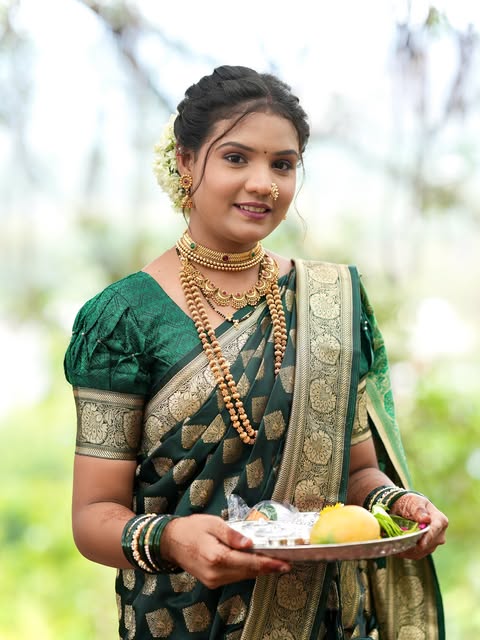 Outdoor bridal portrait in a deep green sari with gold jewellery and a traditional ceremonial tray, from Pooja Salunkhe Makeover's portfolio